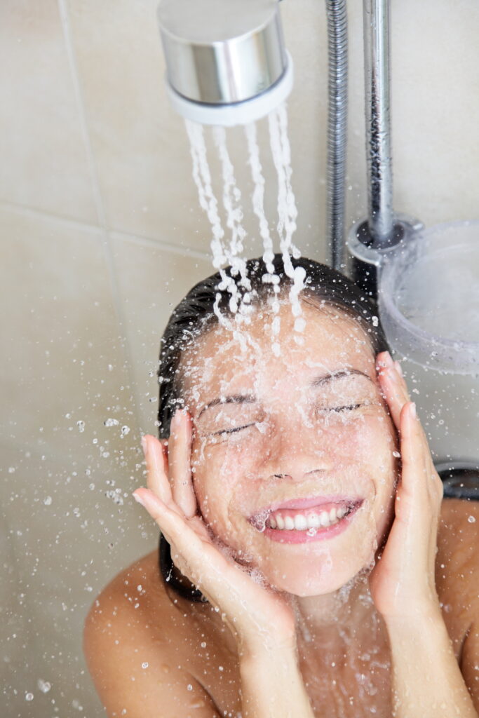 Lächelnde Frau unter fließendem Duschwasser – Symbolbild für Erfrischung an heißen Tagen