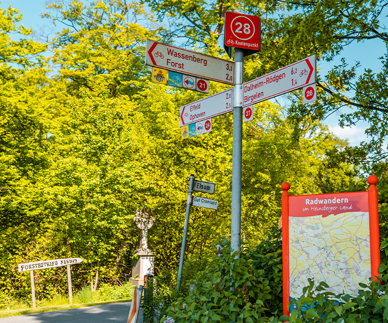 Fahrradwegweiser mit Entfernungsangaben zu Wassenberg, Forst, Birgelen und weiteren Orten am Knotenpunkt 28, daneben eine Radwandertafel des Heinsberger Lands.