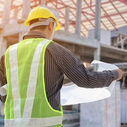 Ein Bauleiter mit Schutzhelm und Sicherheitsweste hält Baupläne auf einer aktiven Baustelle – Symbolbild für die temporäre Stromversorgung mit Baustrom