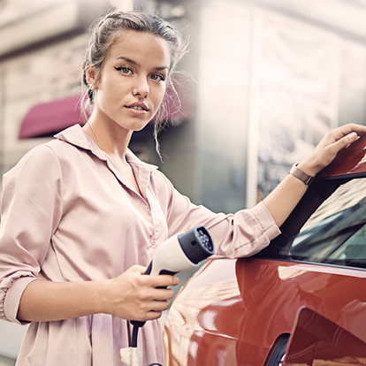 Eine junge Frau lädt ihr Elektroauto an einer Ladestation in der Stadt – Symbolbild für moderne, nachhaltige Mobilität mit Strom der Stadtwerke Willich