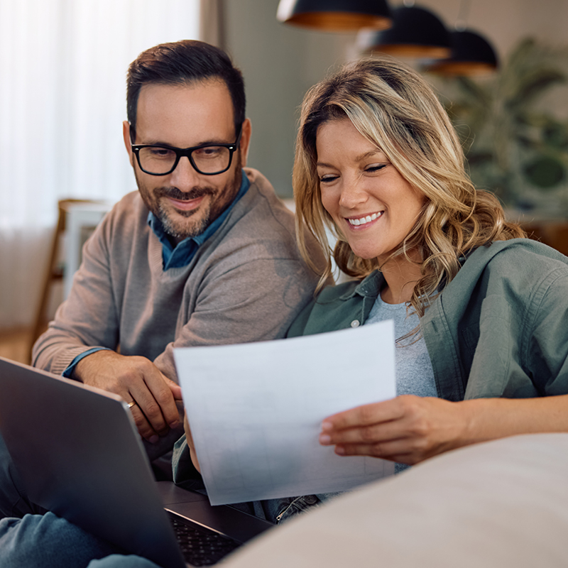 Ein Paar sitzt auf dem Sofa, lächelt und prüft gemeinsam Stromrechnungen – Symbolbild für transparente Energiepreise und Kundennähe