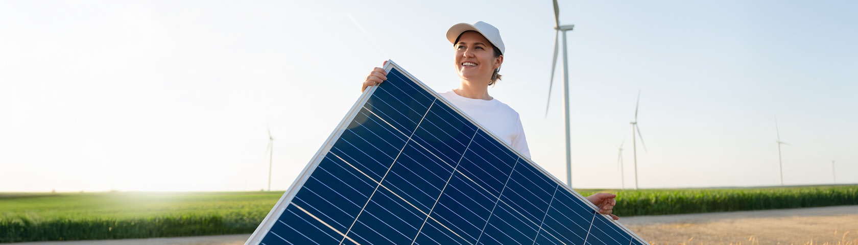Frau trägt Solarmodul auf Feld mit Windrädern im Hintergrund