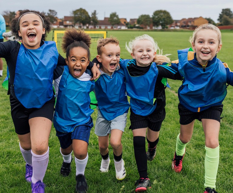 Fünf Kinder rennen lachend über ein Spielfeld und zeigen Teamgeist bei einem Sportprojekt in Willich.