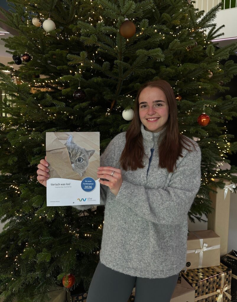 Person hält Familienkalender mit Tiermotiven vor großem Weihnachtsbaum bei Stadtwerke Willich