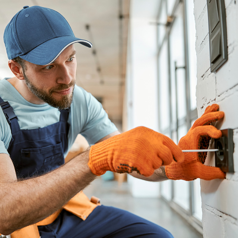 Handwerker mit orangenen Handschuhen prüft Elektrozähler an Hauswand