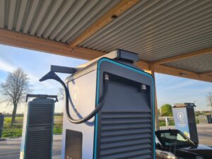 Elektroladestation mit Kabel und Parkplätzen im Hintergrund unter blauem Himmel